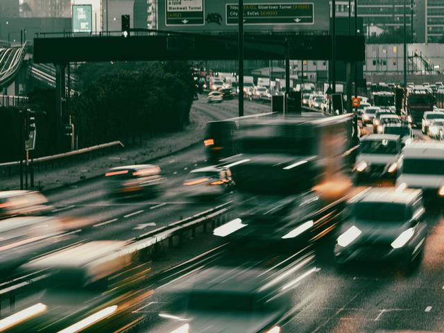 Una vista de tráfico en una carretera urbana con vehículos en movimiento y señales visibles.
