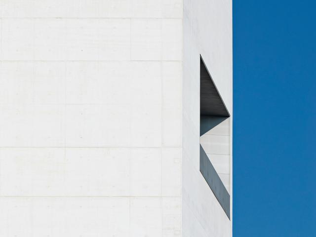 La imagen muestra una esquina de una estructura arquitectónica moderna con una ventana angular y un fondo azul claro.