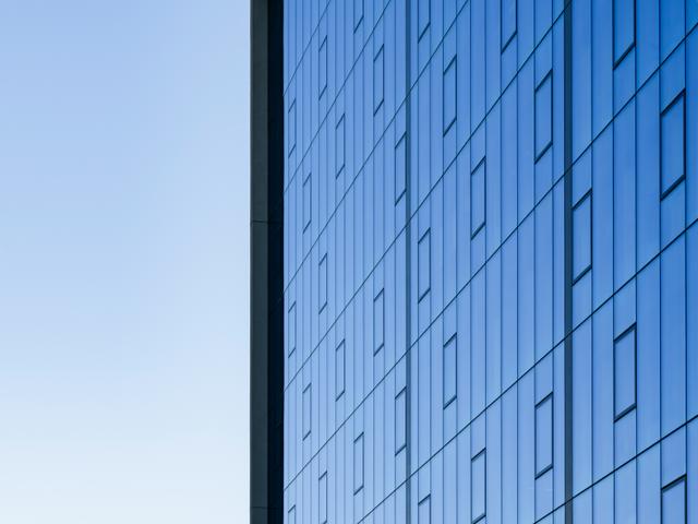 Una vista de un edificio moderno con una fachada de vidrio reflectante y un cielo claro al fondo.