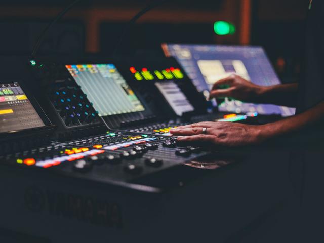 Una persona está ajustando un panel de control de sonido con múltiples botones y pantallas.