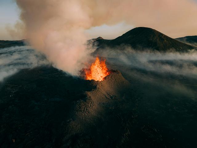 Un volcán en erupción con lava y humo en un paisaje árido.