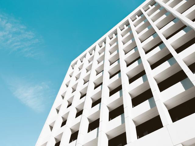 Una vista angular de un edificio moderno con una fachada de paneles blancos y un cielo azul claro.