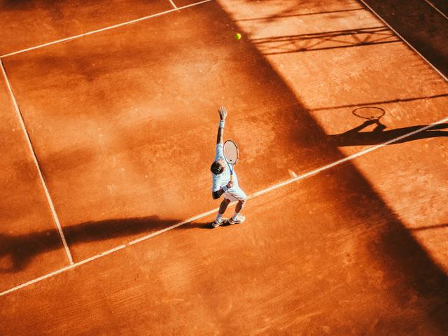 Un jugador de tenis sirve la pelota en una cancha de tierra batida.