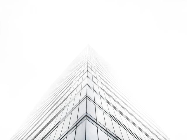 Un rascacielos se eleva en la niebla, con una perspectiva desde abajo que acentúa su altura.