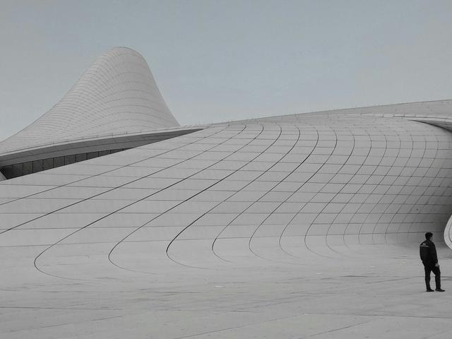 Un hombre se encuentra de pie frente a una arquitectura moderna con formas curvas y minimalistas.