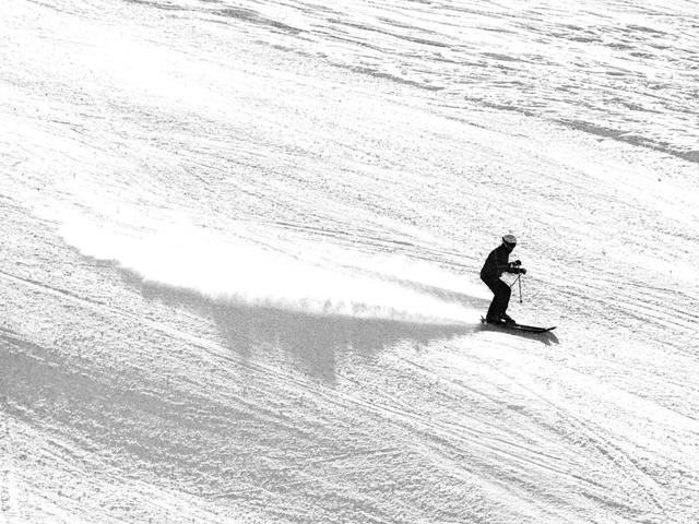 Un esquiador desciende por una pista nevada dejando una estela de nieve.