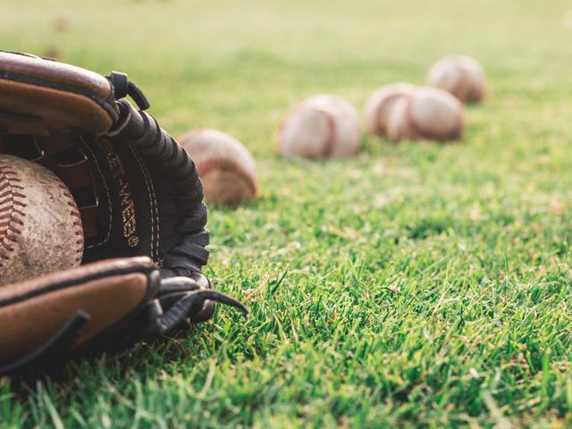 Un guante de béisbol con una pelota, situado sobre un campo de hierba, junto a varias pelotas más en el suelo.