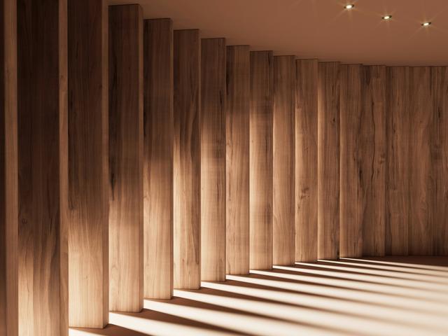 Una sala iluminada suavemente con columnas de madera que proyectan sombras alargadas en el suelo.