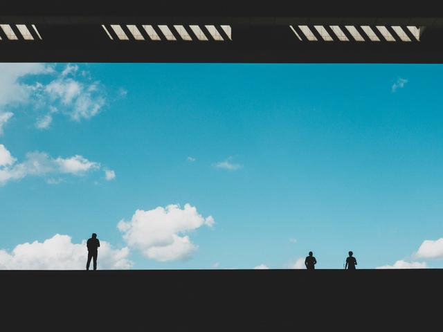 Un grupo de siluetas de personas se observa contra un fondo de cielo azul con nubes esponjosas.