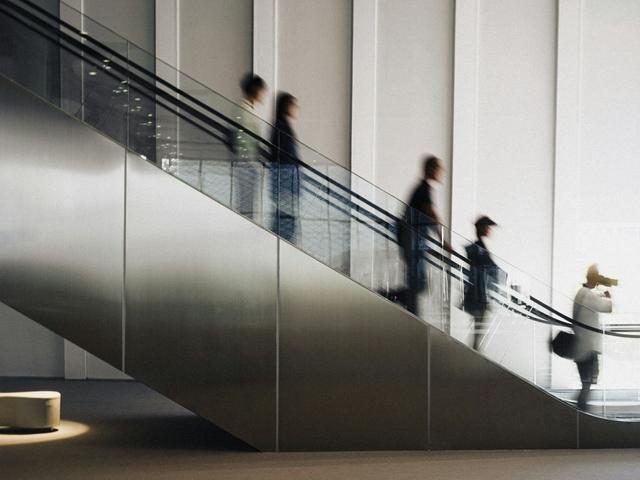 Una imagen que muestra a varias personas bajando por una escalera mecánica en un entorno moderno y minimalista.