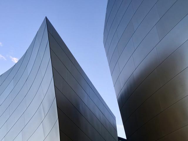 La imagen muestra dos estructuras arquitectónicas metálicas con formas curvadas contra un cielo azul.