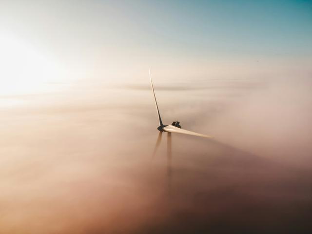 Una turbina eólica sobresale de un mar de niebla bajo un cielo despejado.