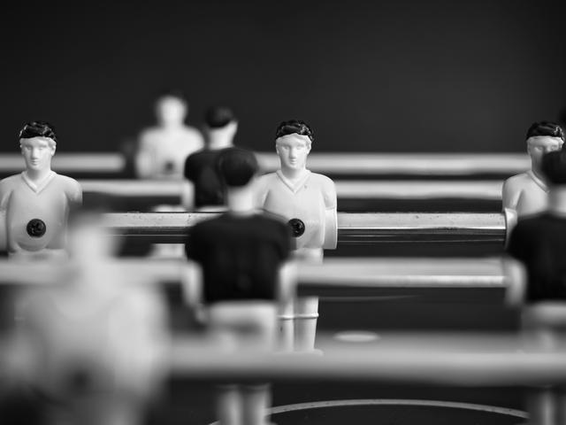 La imagen muestra un juego de futbolín con figuras en blanco y negro dispuestas en alineación.