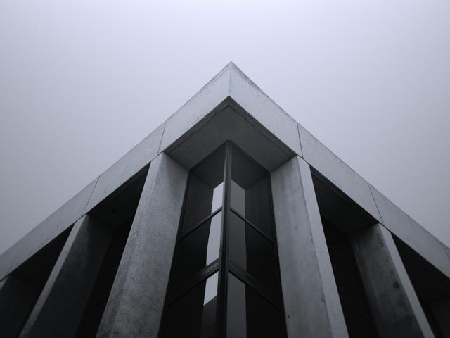 La imagen muestra la esquina superior de un edificio moderno con un diseño minimalista y un ambiente neblinoso.
