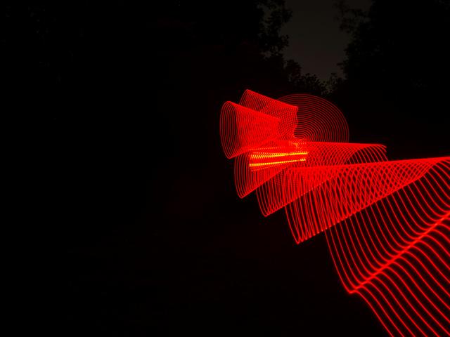La imagen muestra un patrón de luces rojas en movimiento sobre un fondo oscuro.