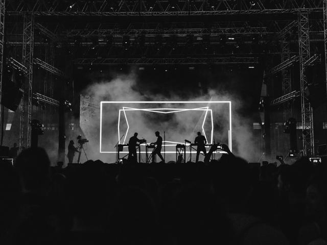 Una presentación musical en un escenario iluminado con efectos visuales en blanco y negro.