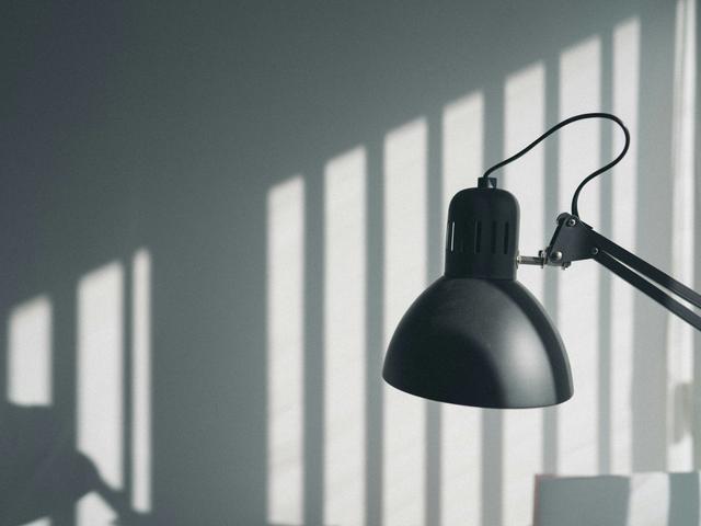 Una lámpara negra emite luz mientras proyecta sombras en la pared.