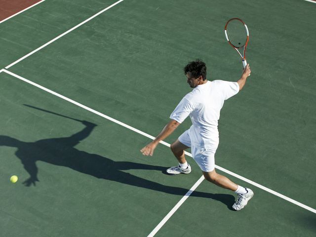 Un jugador de tenis golpea una pelota en una cancha verde.