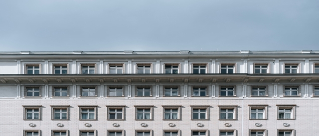 La imagen muestra la fachada de un edificio con varias ventanas y un cielo nublado.