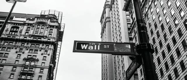 Una señal de calle que dice 'Wall St' entre edificios altos en blanco y negro.