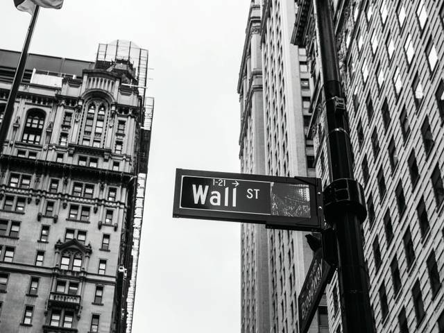 Una señal de calle que dice 'Wall St' entre edificios altos en blanco y negro.