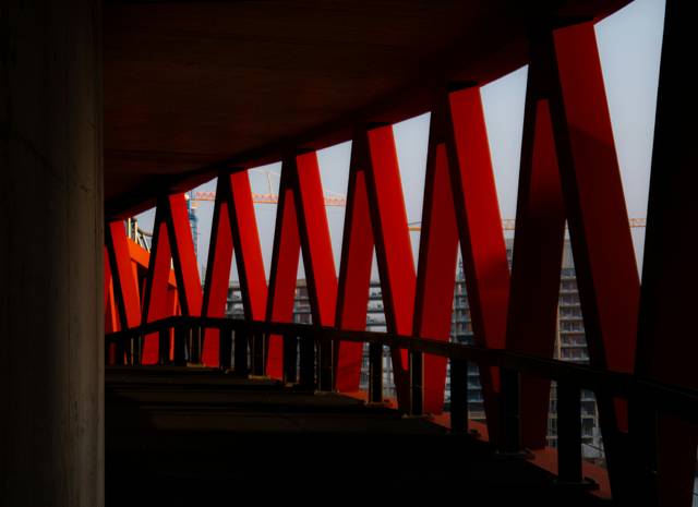 Una estructura arquitectónica con soportes rojos y un pasillo oscuro que muestra edificios en construcción al fondo.