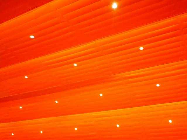 La imagen muestra un techo con paneles de color naranja y luces brillantes distribuidas uniformemente.