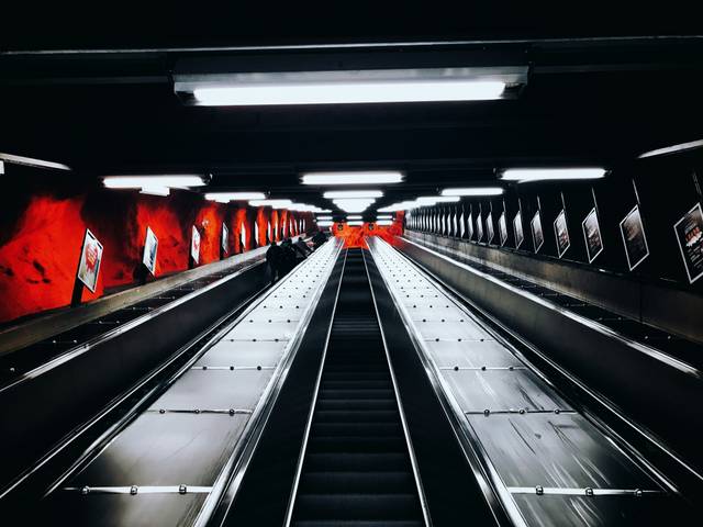 Una escalera mecánica en un entorno urbano con paredes rojas y luces brillantes.