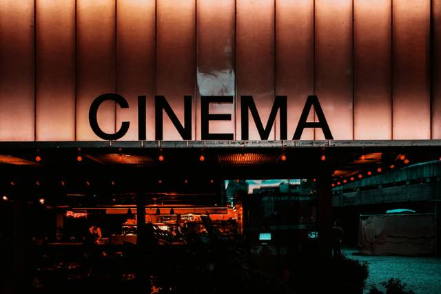 Una fachada de cine iluminada con luces cálidas y un gran letrero que dice 'CINEMA'.