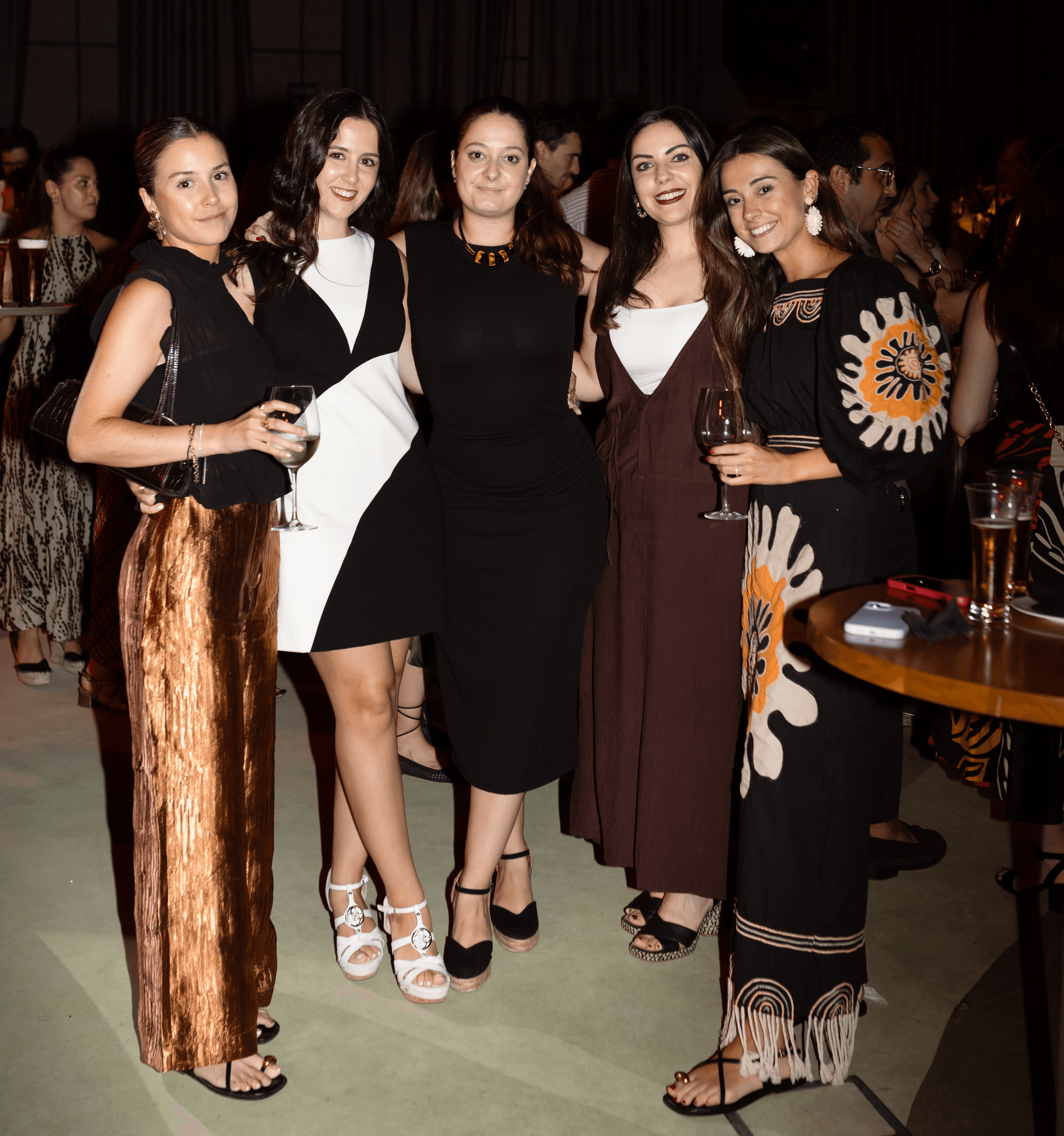 Un grupo de cinco mujeres posando en un evento social con trajes elegantes.